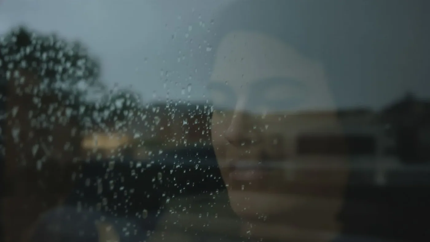 Closed eyes reflected in rain-streaked window illustrating why can't I cry and guarded tears