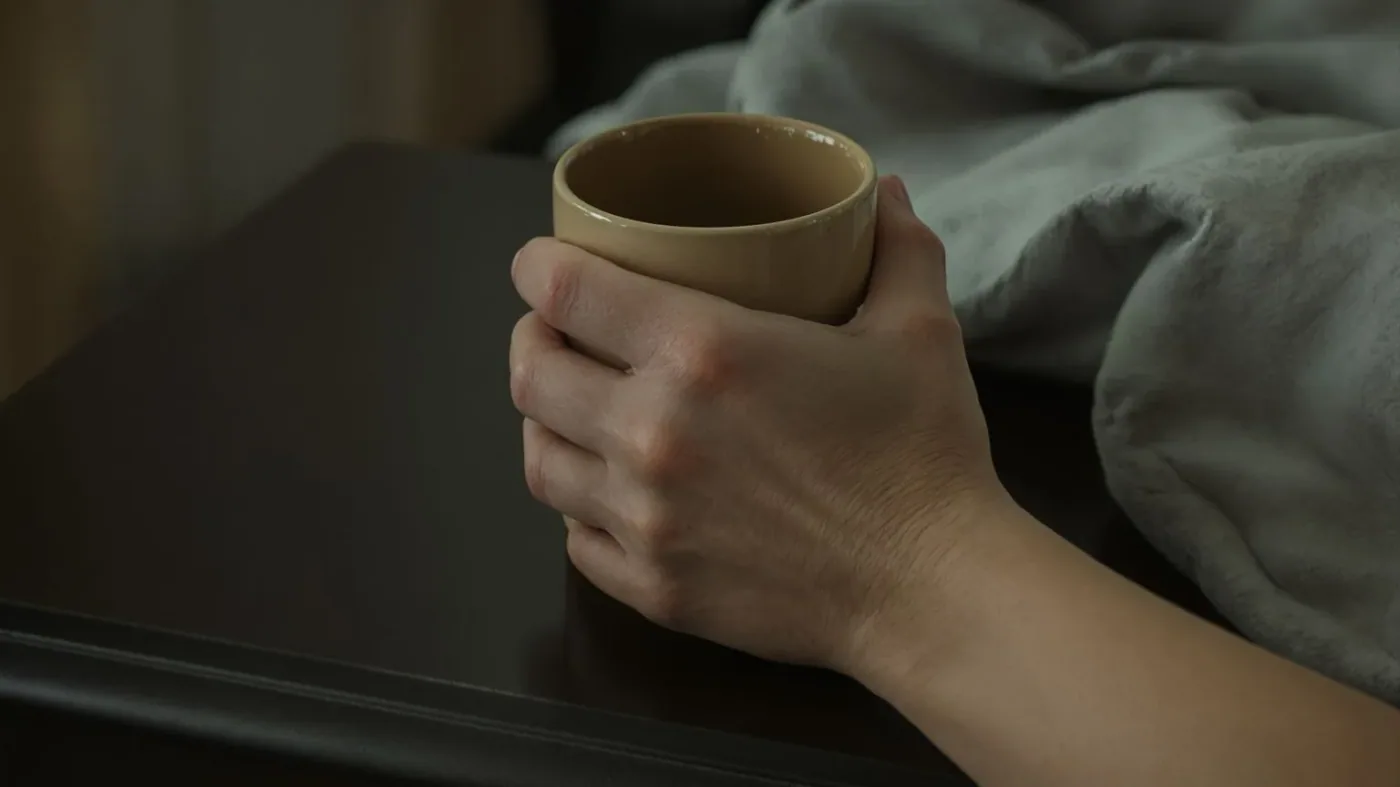 Hands tightly gripping a ceramic mug on a nightstand showing why the body resists just think positive