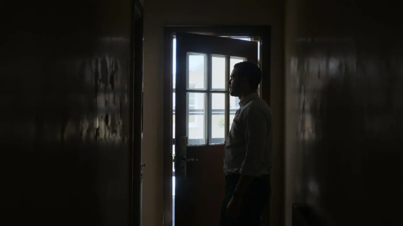 Man hesitating at doorway threshold with hand near chest showing the invisible wall the body notices first