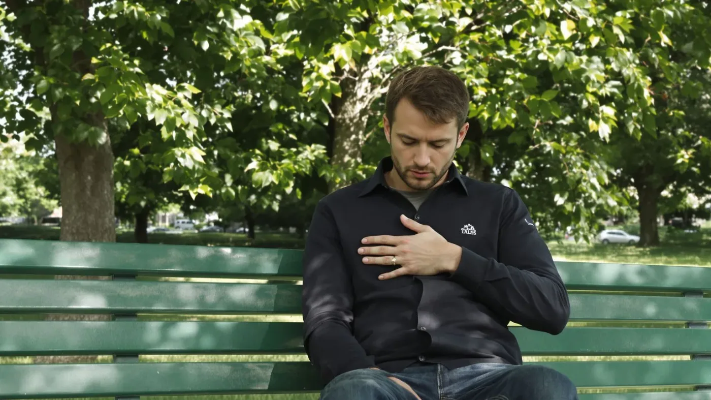 Man on a park bench with hand on chest reading body signals using somatic grounding techniques