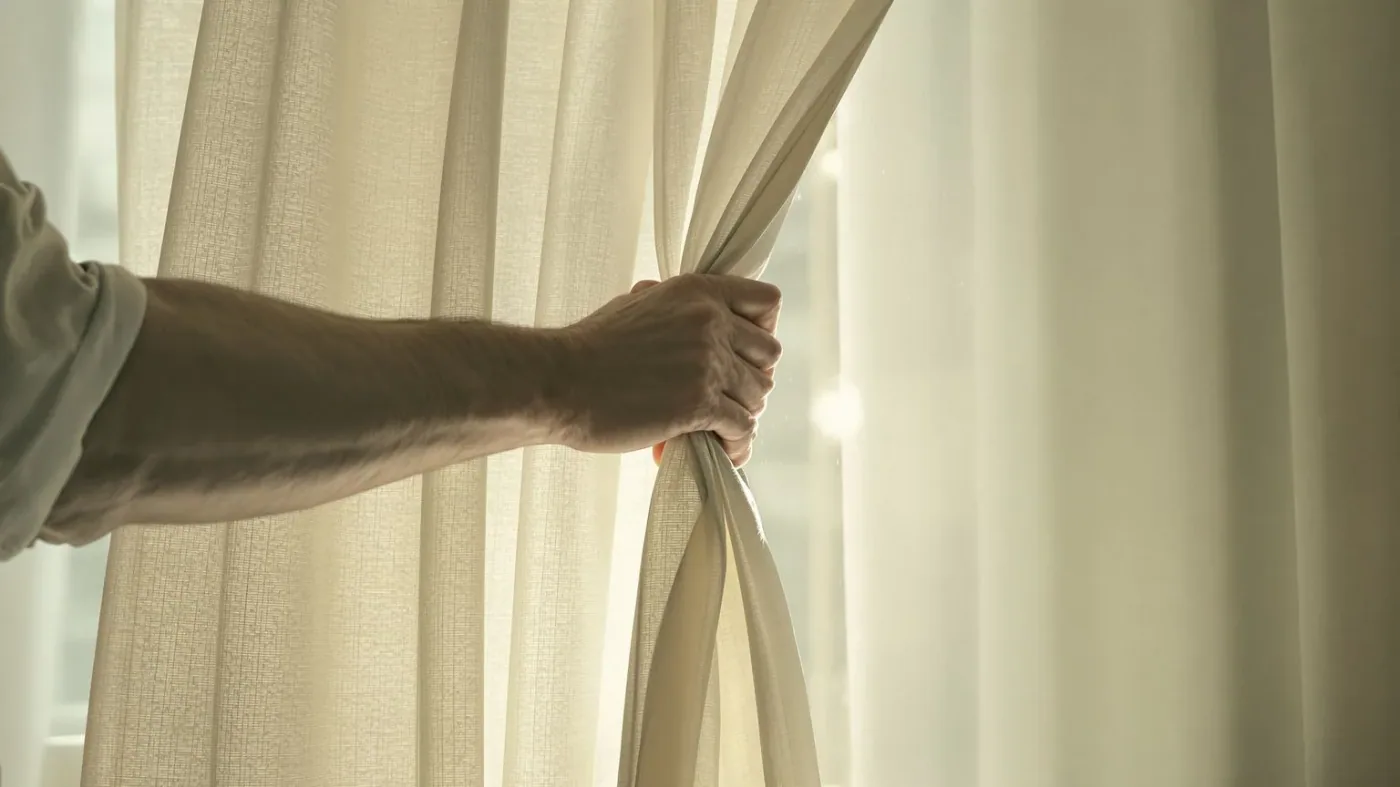 Man pulling back heavy curtain to let morning light in showing body leaning toward emotional opening