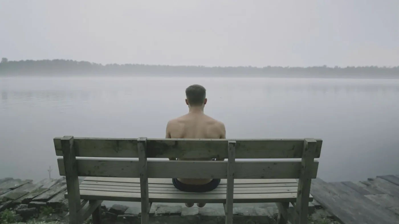 Man's back and posture releasing tension on lakeside bench showing link between suppressing emotions and physical symptoms