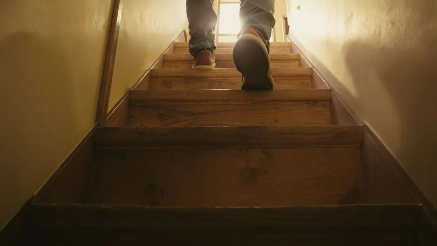 Man's feet paused on worn wooden staircase showing difficulty of trusting yourself through emotional suppression
