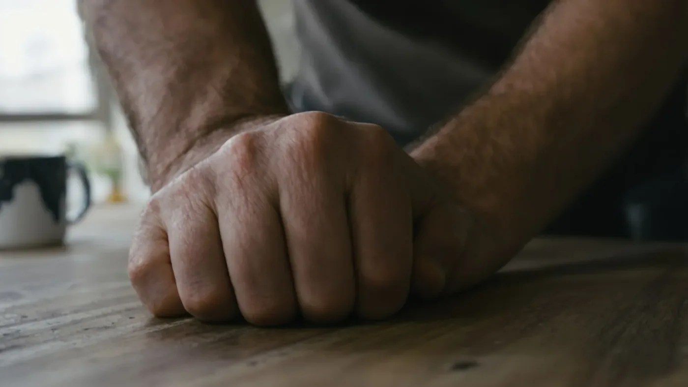 Man's tense hands gripping kitchen table edge showing fear that stays even when wanting connection