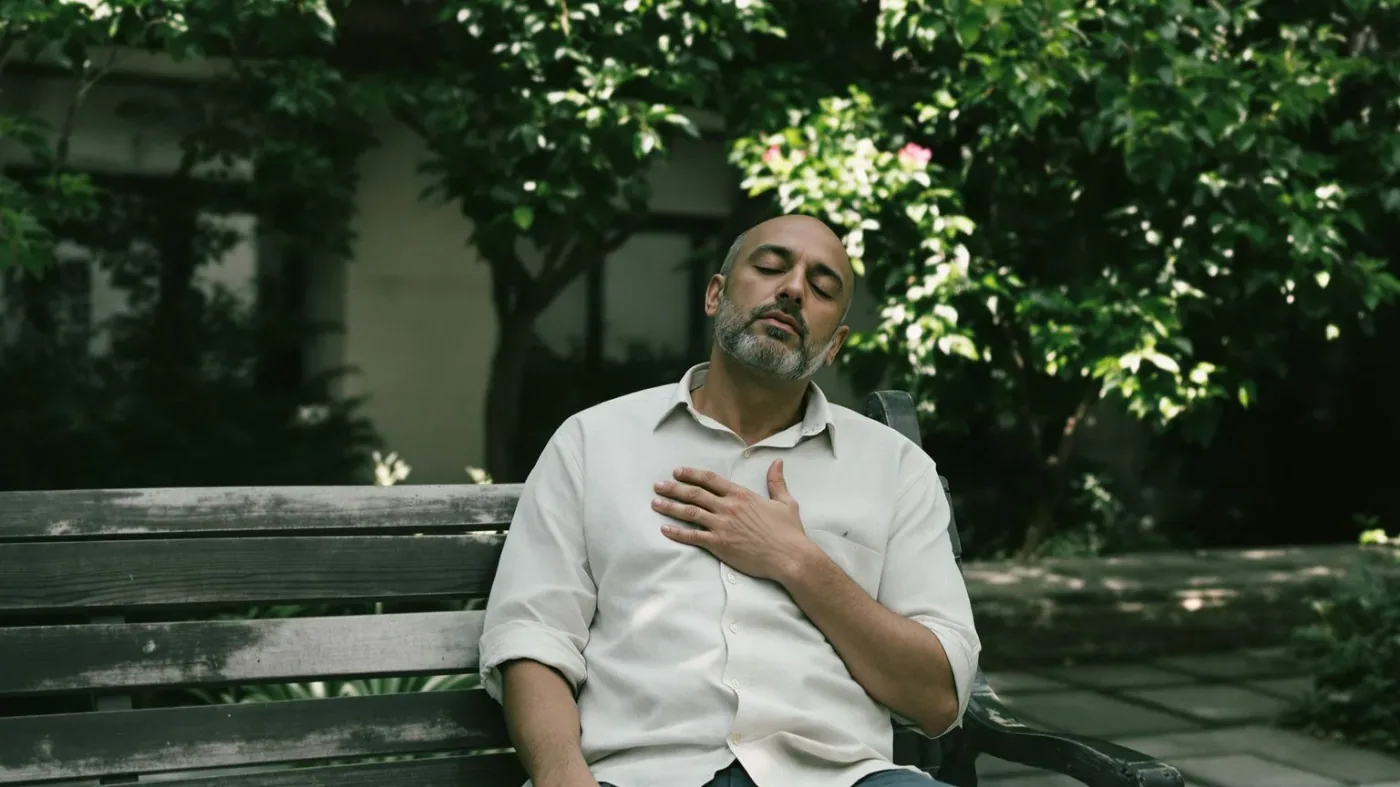 Man sitting on outdoor bench with hand on chest practicing 7-day clarity body awareness exercise