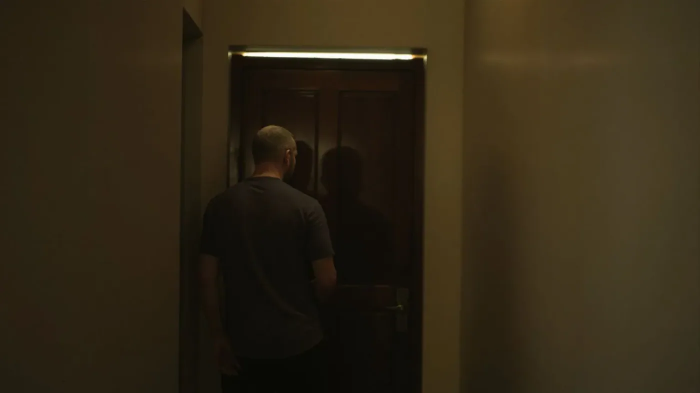 Man standing before closed door with light beneath it showing why emotional suppression patterns repeat
