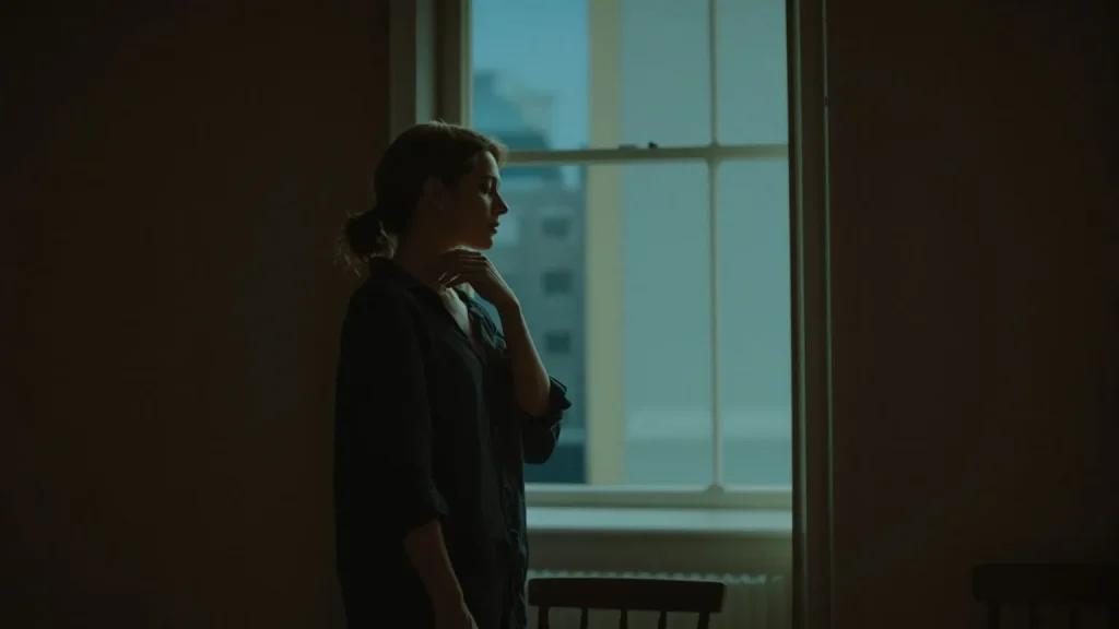 Woman touching her neck near a window at dusk, body slowing down before somatic exercises to release trauma free